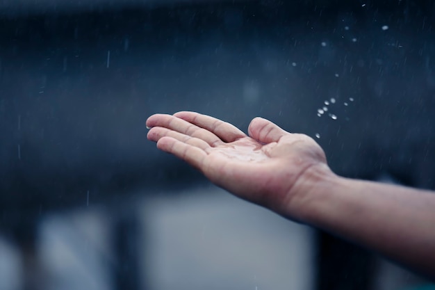 Mano de hombre atrapando gotas de lluvia.