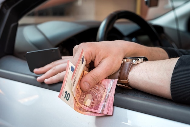 Mano de hombre con billetes en euros y llave dentro del coche para comprar o alquilar. Finanzas