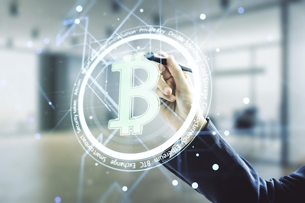 Mano de hombre con bolígrafo trabajando con holograma Bitcoin virtual sobre fondo de oficina borroso Multiexposición