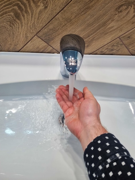 La mano de un hombre bajo un chorro de agua del grifo del lavabo