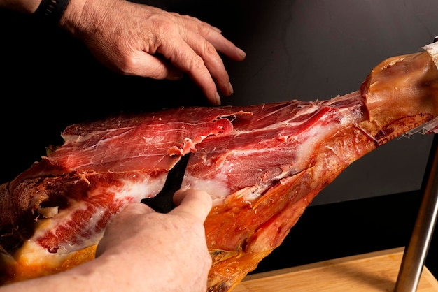 La mano de un hombre corta pedazos delgados de jamón seco de una pierna entera con un cuchillo cocinando comida española