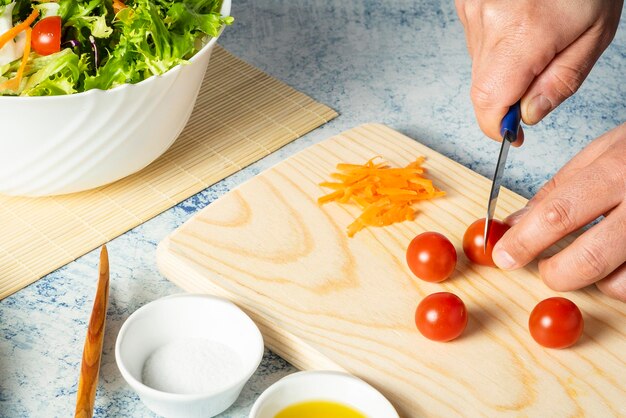 La mano del hombre cortando tomates pequeños en una tabla de madera para colocarlos en una ensalada verde saludable