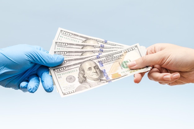 La mano del hombre dando dólares de dinero a una mano en guante quirúrgico azul enfermera o médico Corrupción en el campo de la medicina