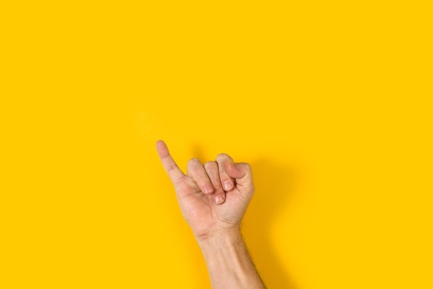 Mano de hombre con el dedo meñique levantado sobre un fondo amarillo