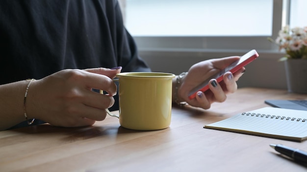 Mano de hombre elegante sosteniendo una taza de café y usando un teléfono móvil en una mesa de madera