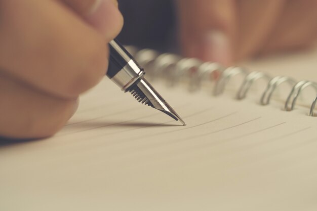 Mano del hombre con la escritura de la pluma en el cuaderno. De cerca