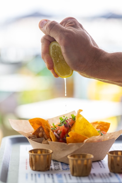 La mano de un hombre exprime jugo de limón en una tradicional buldosalsa de nachos mexicanos