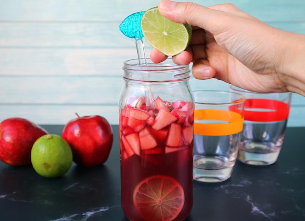 Foto la mano de un hombre exprimiendo una rebanada de lima en la botella de sangria de vino rojo