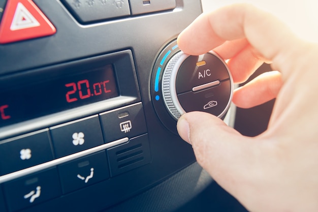 La mano del hombre fijó la temperatura del aire acondicionado en el coche. Conductor que enciende el sistema de control de clima del automóvil. viajar en automóvil. Vista cercana con enfoque selectivo.