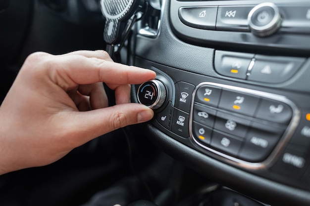 La mano del hombre gira la rueda del control de clima en un coche Ajuste de temperatura