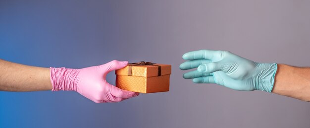 La mano de un hombre en un guante azul está dando una caja de regalo a la mano de una mujer en un guante rosa