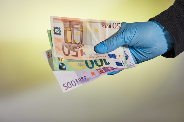 La mano de un hombre con un guante médico azul tiene dinero en forma de billetes en una tabla amarilla. Protección contra virus y bacterias.