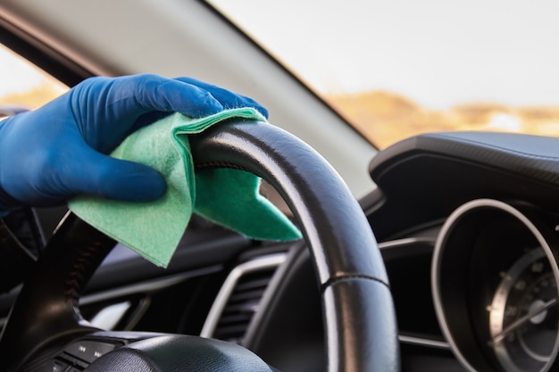 La mano del hombre en guante protector azul está limpiando el volante con un paño.