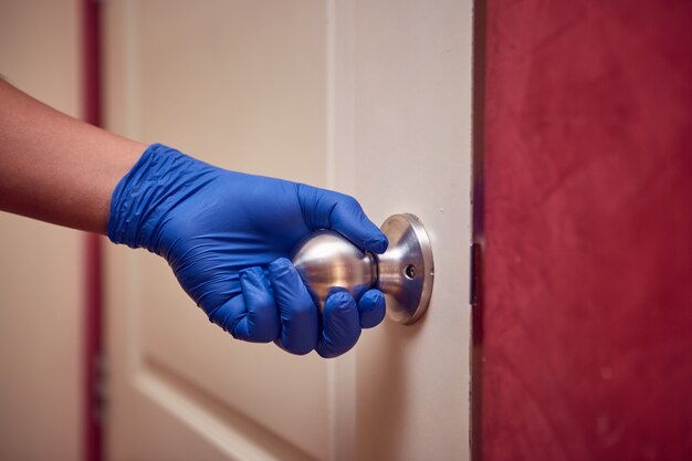 la mano de un hombre con guantes de nitrilo abre la puerta tocando la perilla