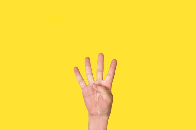 Mano de hombre haciendo el gesto número cuatro sobre un fondo amarillo con espacio de copia