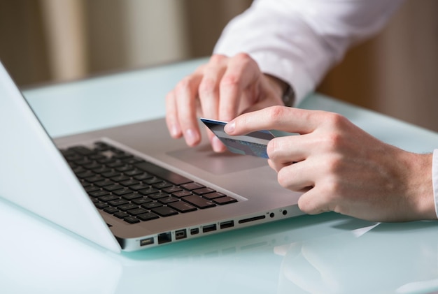 La mano del hombre ingresando datos usando una computadora portátil mientras sostiene una tarjeta de crédito en la otra mano