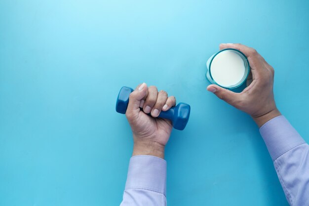 Foto mano de hombre joven sosteniendo mancuernas y vaso de leche en azul