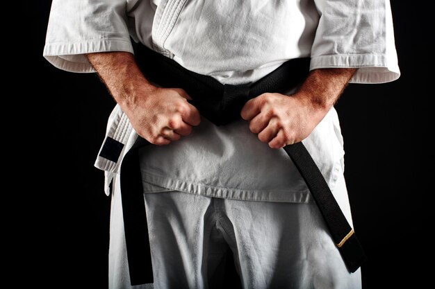 La mano de un hombre en kimono, atando el cinturón sobre fondo negro