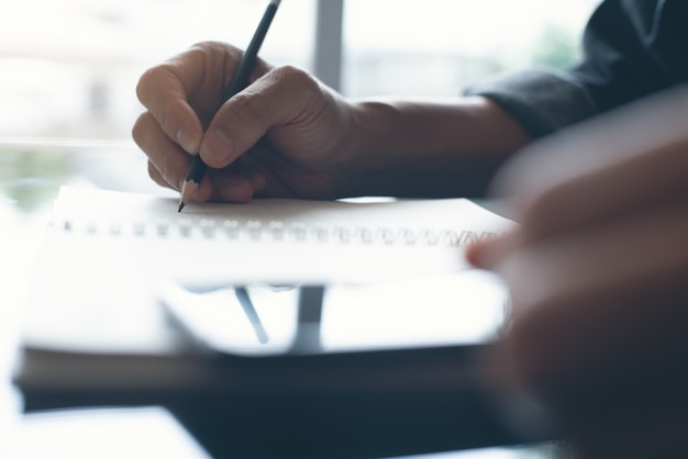 Mano del hombre con un lápiz escribiendo en el bloc de notas