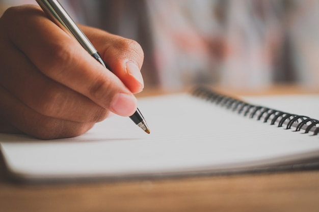 Mano de hombre con lápiz escribiendo en el cuaderno. Tomate de la mano con un bolígrafo. Blanco sobre un escritorio, patrones de madera de la naturaleza, escribiendo un libro.