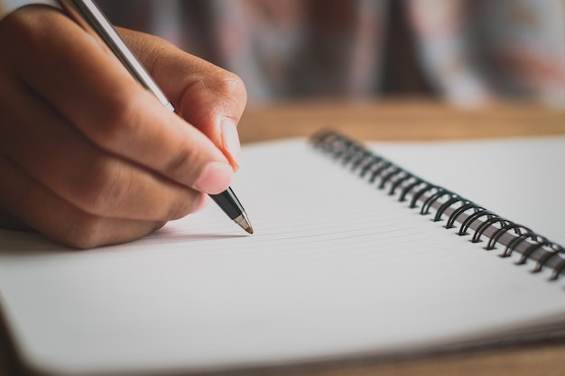 Mano de hombre con lápiz escribiendo en el cuaderno. Tomate de la mano con un bolígrafo. Blanco sobre un escritorio, patrones de madera de la naturaleza, escribiendo un libro.