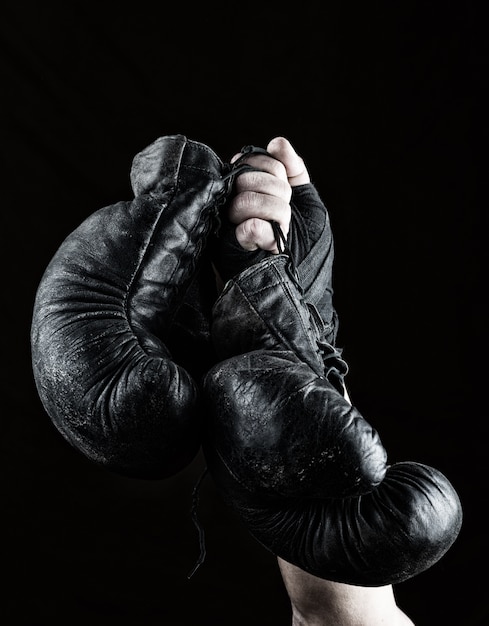 La mano del hombre levantada sostiene un par de viejos guantes de boxeo de cuero negro