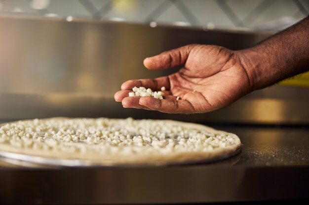 La mano del hombre mientras está poniendo queso rallado sobre la masa antes de hornear