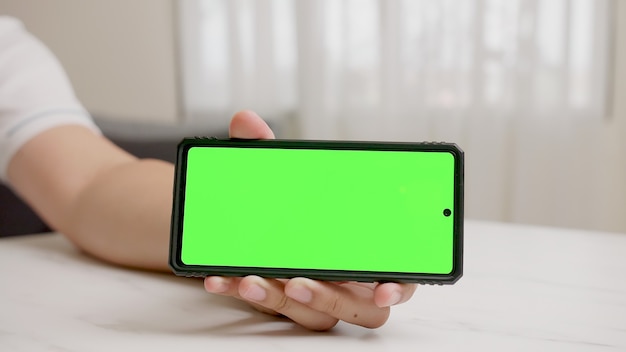 La mano del hombre muestra un teléfono inteligente con pantalla verde en posición horizontal