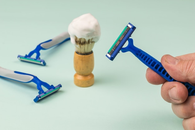 La mano de un hombre con una navaja desechable en el fondo de accesorios de afeitado