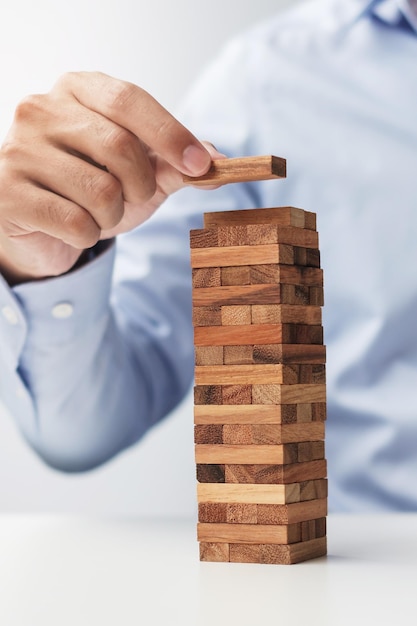 Mano de hombre de negocios colocando o tirando de un bloque de madera en la torre Planificación empresarial Gestión de riesgos Solución y estrategia Conceptos