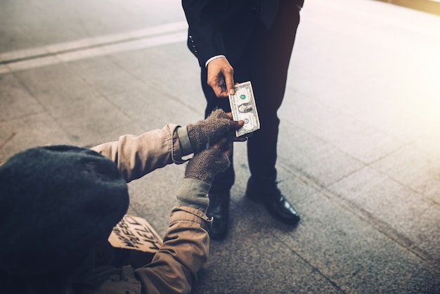 Mano de hombre de negocios dando dólar a mendigo sin hogar en el puente.