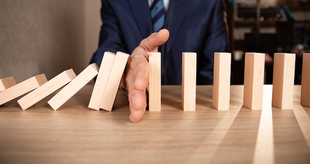 Mano de hombre de negocios detener efecto dominó de madera caída de continuo derrocado o riesgo, estrategia y concepto de intervención exitosa para el negocio.