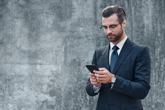 Mano de hombre de negocios elegante sosteniendo y usando un teléfono inteligente al aire libre