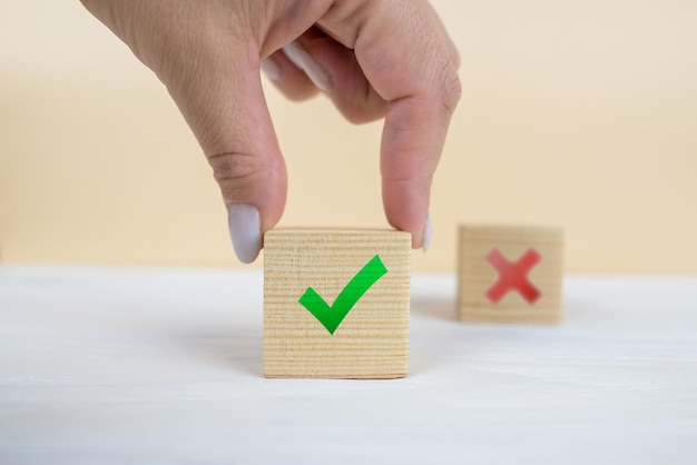 La mano de un hombre de negocios elige la marca de verificación y el símbolo de signo x en un bloque de cubo de madera