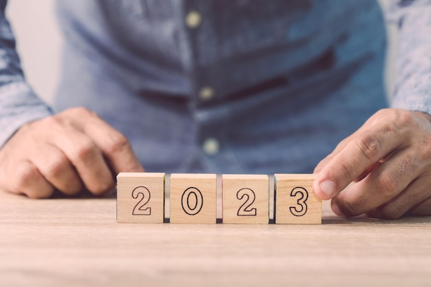 La mano del hombre de negocios está clasificando un dado de madera con el número de 2023 en el concepto de trabajo de mesa en