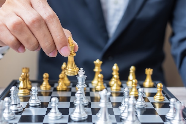 Mano de hombre de negocios moviendo la figura del rey del ajedrez de oro y jaque mate u oponente durante la competencia de tablero de ajedrez.