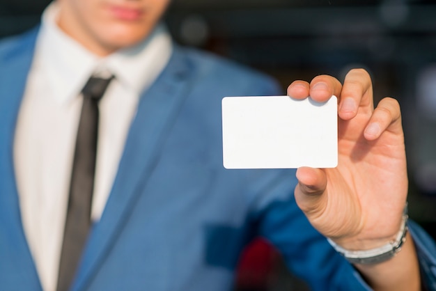 La mano del hombre de negocios que muestra la tarjeta blanca en blanco