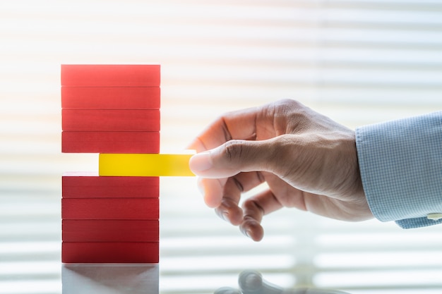 Mano del hombre de negocios que quita el bloque amarillo de la pila de bloques rojos. Concepto de gestión de riesgos empresariales.