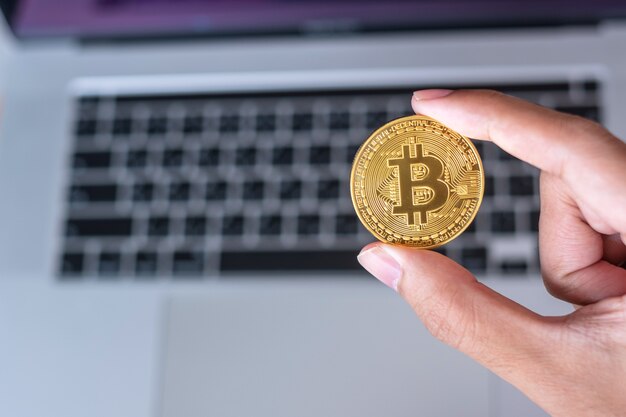 Mano de hombre de negocios que sostiene la criptomoneda dorada de Bitcoin (BTC) sobre el teclado de la computadora portátil, Crypto es dinero digital dentro de la red blockchain, se intercambia utilizando tecnología y concepto de intercambio en línea