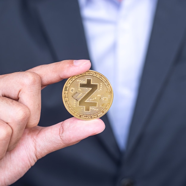 La mano del hombre de negocios que sostiene la moneda de criptomoneda dorada ZCASH (ZEC), Crypto es dinero digital dentro de la red blockchain, se intercambia utilizando tecnología e intercambio de Internet en línea. Concepto financiero