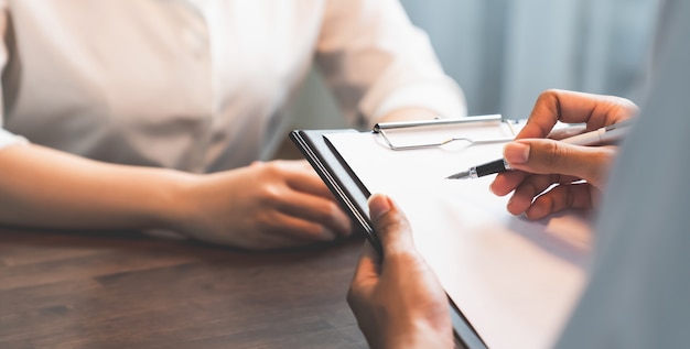 Mano de hombre de negocios que sostiene la pluma poniendo el papel y el borrador del contrato con los clientes.