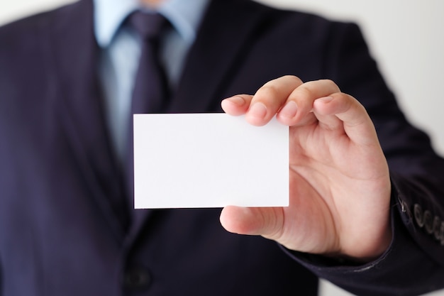 Mano de hombre de negocios que sostiene la tarjeta de visita blanca en blanco con el espacio de la copia para el texto
