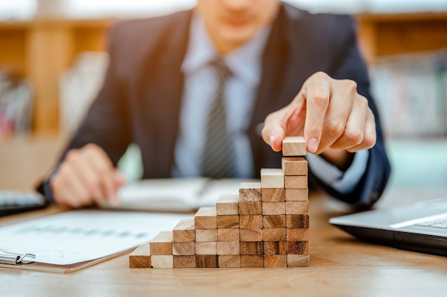 Mano de hombre de negocios sacando o colocando bloques de madera en la torre y semipirámide en la oficina moderna Plan y estrategia en los negocios Conceptos de crecimiento y desarrollo empresarial