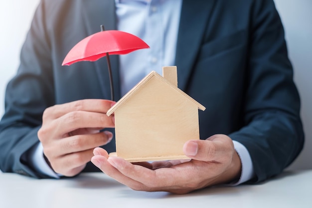 Foto mano de hombre de negocios sosteniendo la cubierta del paraguas rojo conceptos de propiedad y seguros inmobiliarios modelo de casa de madera