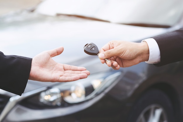 mano de hombre de negocios sosteniendo las llaves del coche frente con coche nuevo, estacionamiento en frente de la casa. concepto de transporte.