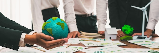 Foto mano de hombre de negocios sosteniendo la tierra de papel con gente de negocios reunida en la planificación de la oficina e implementando un ideal ecológico para la política corporativa para reducir las emisiones de co2 y salvar la tierra