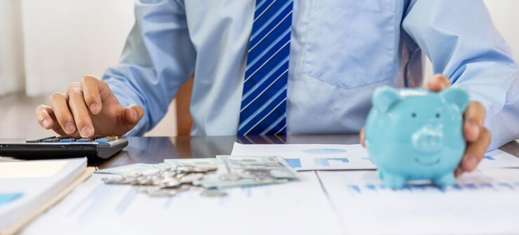 La mano del hombre de negocios usa la calculadora para verificar los ingresos y los gastos en la cuenta con la alcancía y los billetes en dólares aumentan el éxito de las empresas emergentes Ahorrando dinero para el plan futuro y el concepto de fondo de jubilación