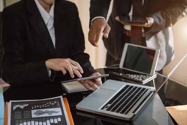 Mano de hombre de negocios usando una computadora portátil y una tableta con diagrama de red social y dos colegas discutiendo datos en el escritorio como concepto en la luz de la mañana