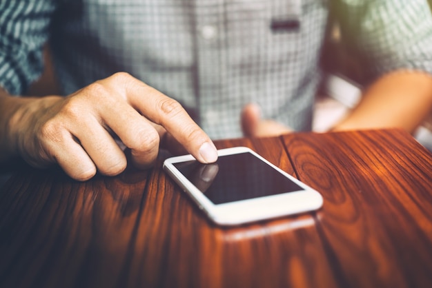 Mano de hombre de negocios usando el teléfono móvil en la cafetería en la luz de la mañana