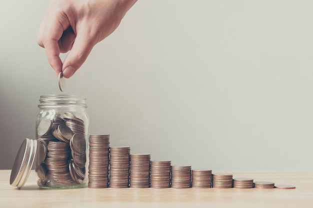 Mano de hombre o mujer poniendo monedas en tarro con dinero pila paso crecimiento ahorrar dinero